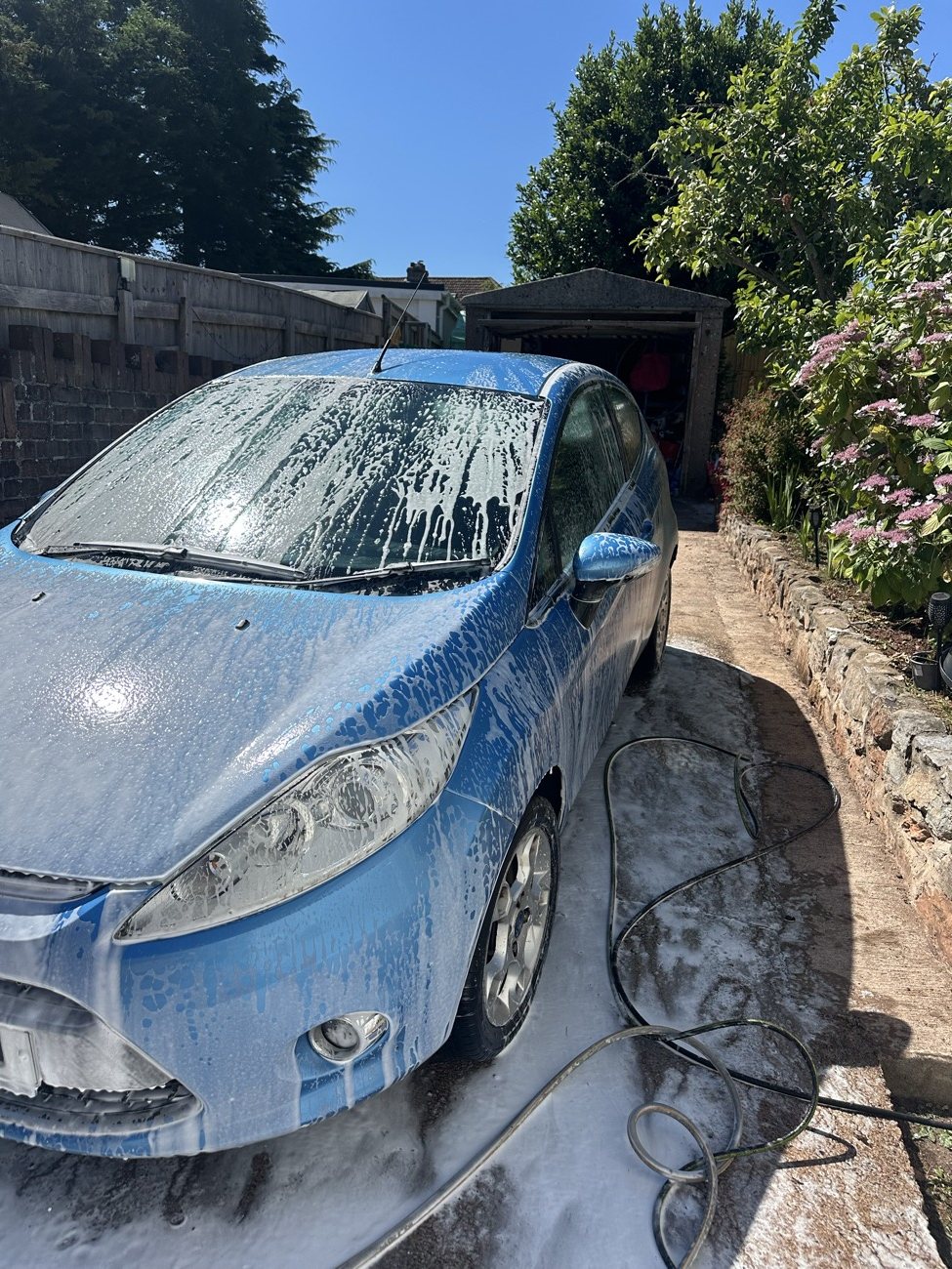 Blue Ford Fiesta covered in snow foam before rinsing